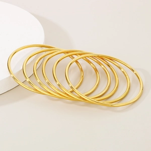 Close-up of seven stacked minimalist gold titanium steel bangles with a polished finish