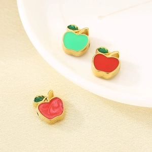 Macro shot of three apple-shaped enamel charms with gold edges in green and red colors