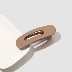 Macro shot of a matte brown large duckbill hair clip on a minimalist white ceramic plate