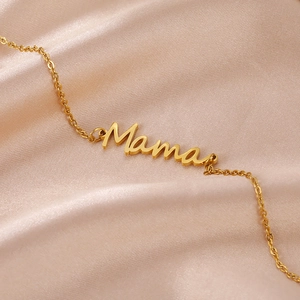 Macro detail of gold-plated Mama letter pendant on stainless steel chain on silk