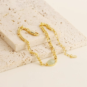 Close-up of a gold chain bracelet with a green aventurine stone on a beige stone base