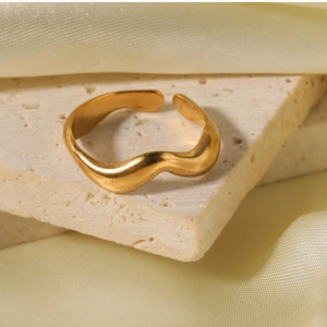 Close-up of wavy gold plated stainless steel open ring on a textured stone surface