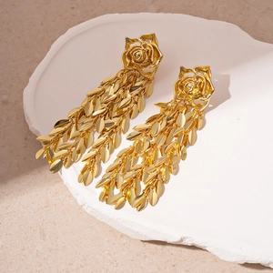 Detailed macro view of golden rose and leaf tassel drop earrings on white stone tray