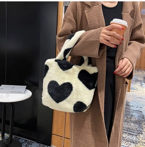 Detail of soft heart print plush tote bag held by model in modern indoor setting