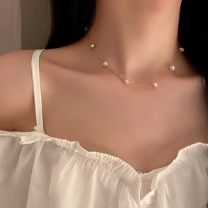 Close-up of a gold thin chain necklace featuring spaced pearls on a model wearing white