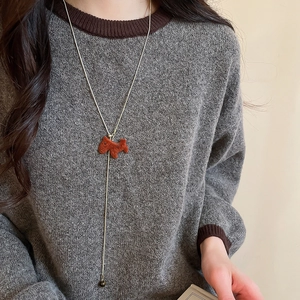Detail of a brown flocked puppy pendant on a long gold snake chain over a knit sweater