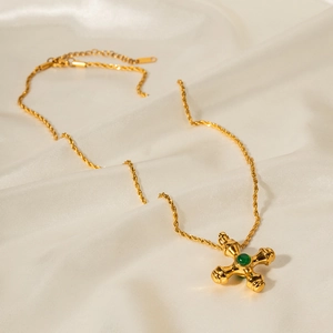 Close-up of 18k gold cross necklace with green gemstone on elegant beige silk