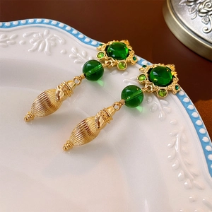 Dettaglio degli orecchini dorati vintage con gemme verdi su un piatto in ceramica