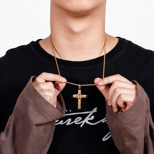 Close-up of golden cross necklace with red inlay and rope chain on a male model