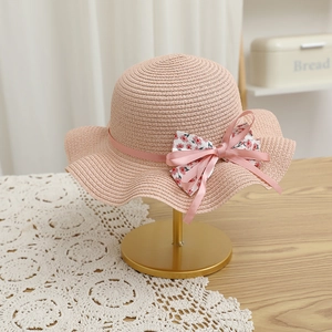 Détail du chapeau de paille rose pour fille avec nœud floral et bordure ondulée