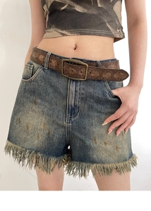 Close-up of vintage embossed brown leather belt with distressed denim shorts