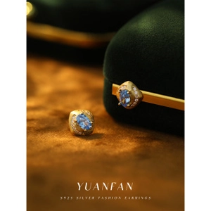 Macro detail of S925 sterling silver earrings with blue oval gemstone on brown velvet