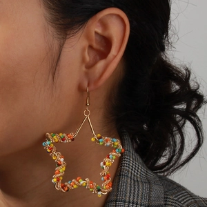 Close-up of oversized star drop earrings with multi-color beads and gold wire frame