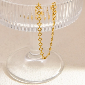 Close-up of golden hollow heart chain bracelet hanging on textured striped glassware