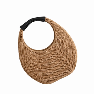 Handwoven straw shoulder bag with moon shape and black leather handles on white background