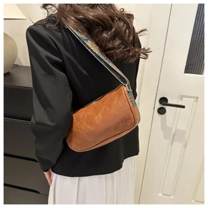 Brown leather shoulder bag with floral strap shown on model in indoor setting