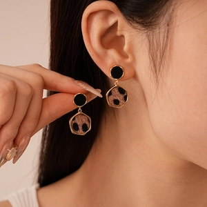 Close-up of leopard print hexagonal earrings with gold trim and black studs on a model