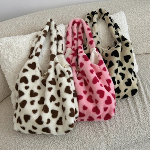 Three plush heart-patterned tote bags in different colors displayed on a cozy sofa