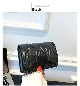 Close-up of black glossy heart-shaped buckle and gold chain strap on a mini bag