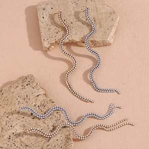 Macro shot of gold and silver S-shaped wave tassel earrings with sparkling zircons
