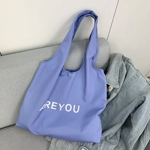 Close-up of a blue canvas tote bag with white AREYOU text on a gray sofa next to denim