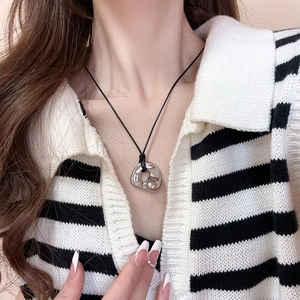 Close-up of a silver irregular heart pendant on a black cord necklace worn on the neck