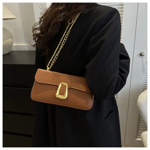 Detailed view of brown crossbody bag with gold metal clasp and chain strap on model
