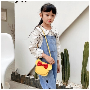 Close-up of a yellow mini cartoon crossbody bag with red bow on a child model