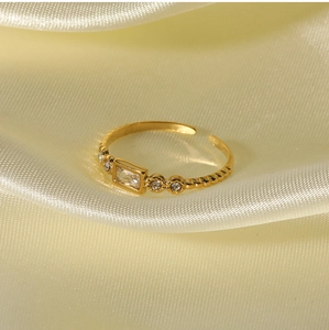 Detailed close-up of a square-cut zircon stone on a twisted gold-plated band over silk