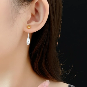 Detail of silver drop earrings with gold studs worn on ear against dark background