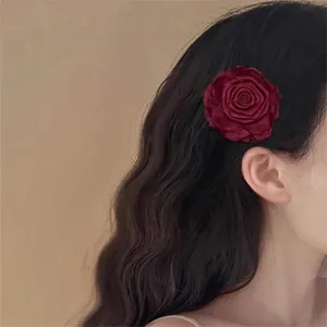 Elegant burgundy fabric rose hair clip with layered petals worn by a model in profile