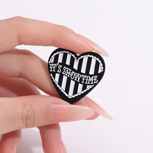 Cartoon heart brooch with black and white stripes and 'IT'S SHOWTIME' text on metal badge