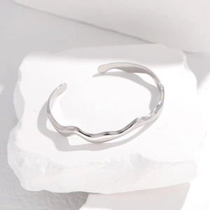 Elegant silver wavy stainless steel cuff bracelet on minimalist stone base display