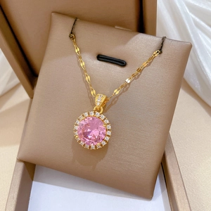 Detail shot of a gold necklace featuring a round pink gem pendant inside a gift box