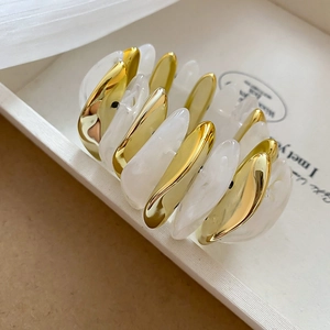 Detailed close-up of golden metal and marbled white resin oval links of the acrylic bracelet