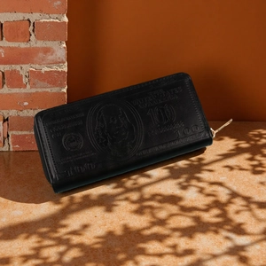 Macro shot of black leather wallet featuring embossed 100 dollar bill and gold zipper