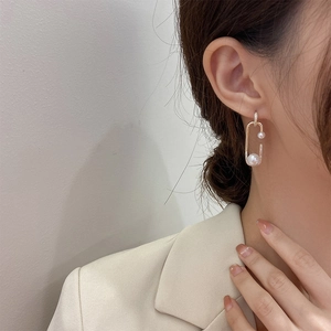 Detail of gold paperclip drop earring with pearl and rhinestones worn by a model
