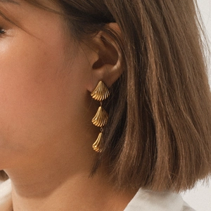 Close-up of a model wearing three-tier golden shell earrings with a fringe design