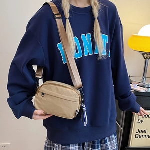 Detail of khaki nylon crossbody phone bag with wide strap worn by model in cozy room