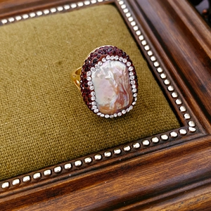 Detail of vintage gold-plated ring with baroque pearl and garnet-colored crystals