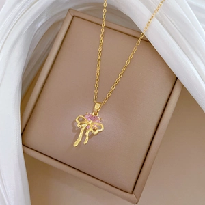 Macro shot of gold bow pendant with pink heart crystal on beige jewelry display
