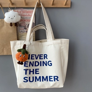Detail of off-white canvas tote bag with navy text print and orange persimmon plush charm