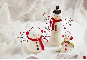Three sizes of handmade wool felt snowmen Christmas decorations on soft white fabric