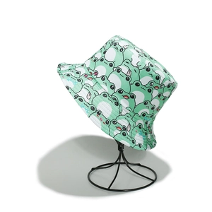 Detail of light green bucket hat with cartoon frog patterns on a black metal display stand