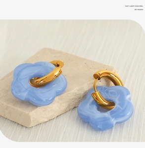 Detail of blue marble resin flower earrings with gold metal hoops on stone base