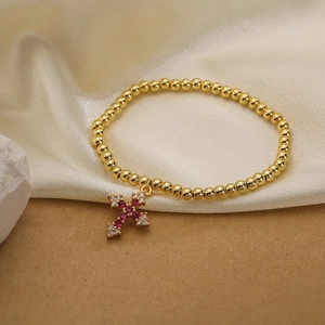 Detail of gold beaded bracelet with a rose red and white zircon cross charm on silk