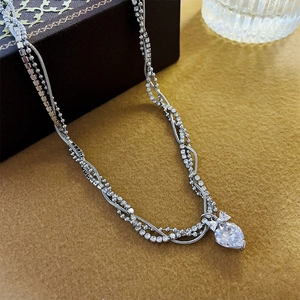 Close-up of layered silver necklace with bow and heart-shaped cubic zirconia stone