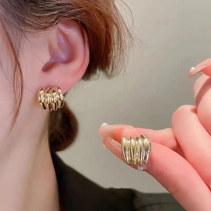 Macro detail of gold wavy earrings showing minimalist wrinkled texture and sleek metallic finish