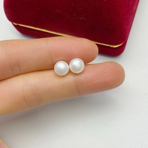 Macro shot of minimalist round white freshwater pearl earrings on red velvet padding