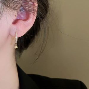 Gros plan de créoles plaquées or avec zircons et une petite perle dorée suspendue